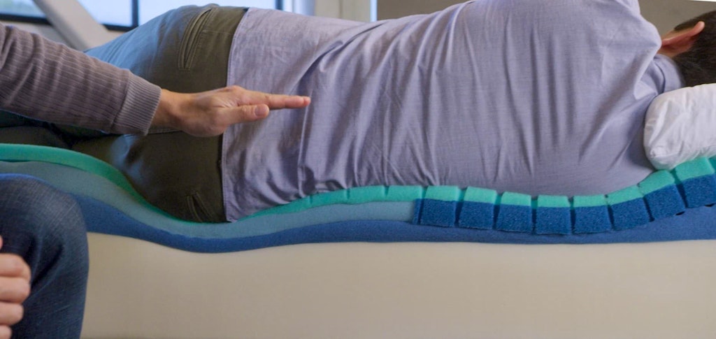 A person lies on a bed while another points at the alignment of their spine.